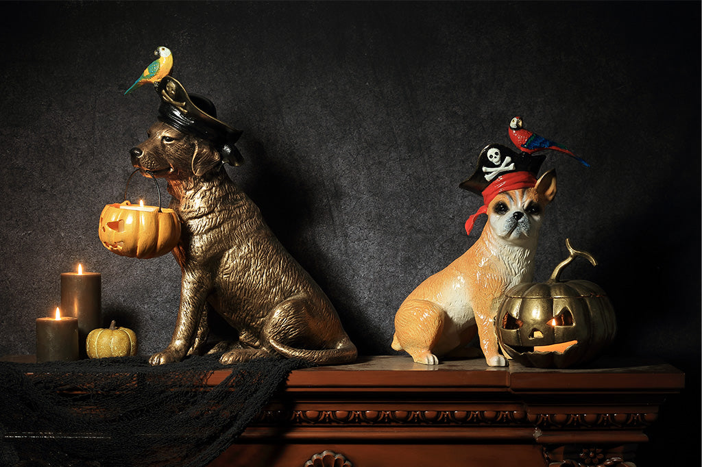 Two cast metal Pirate dog sculptures, each featuring a parrot perched on pirate hat with jack o lantern that holds a candle