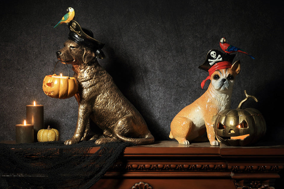 Two cast metal Pirate dog sculptures, each featuring a parrot perched on pirate hat with jack o lantern that holds a candle