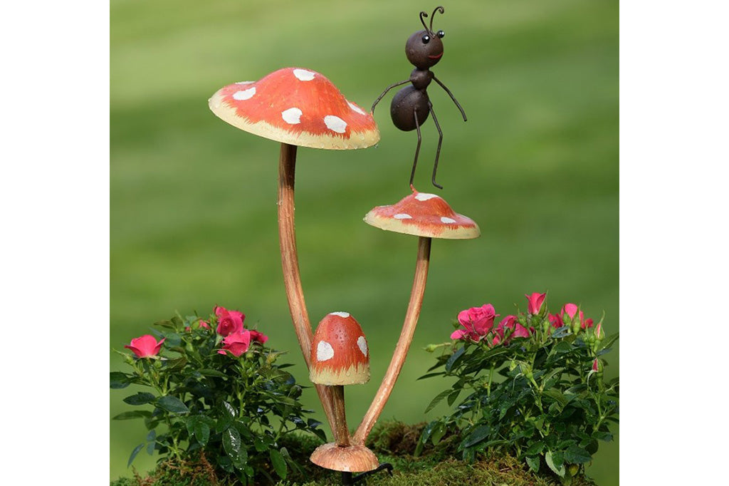 Metal garden accent of one ant frolicking on a trio of mushrooms.