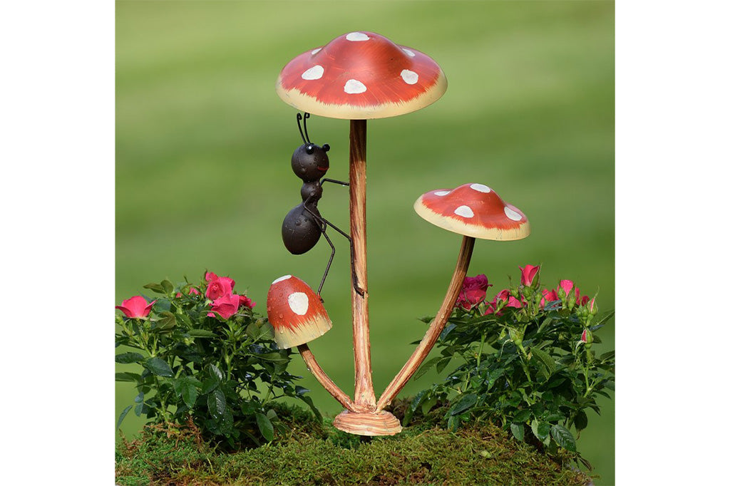 Metal garden accent of one ant frolicking on a trio of mushrooms.