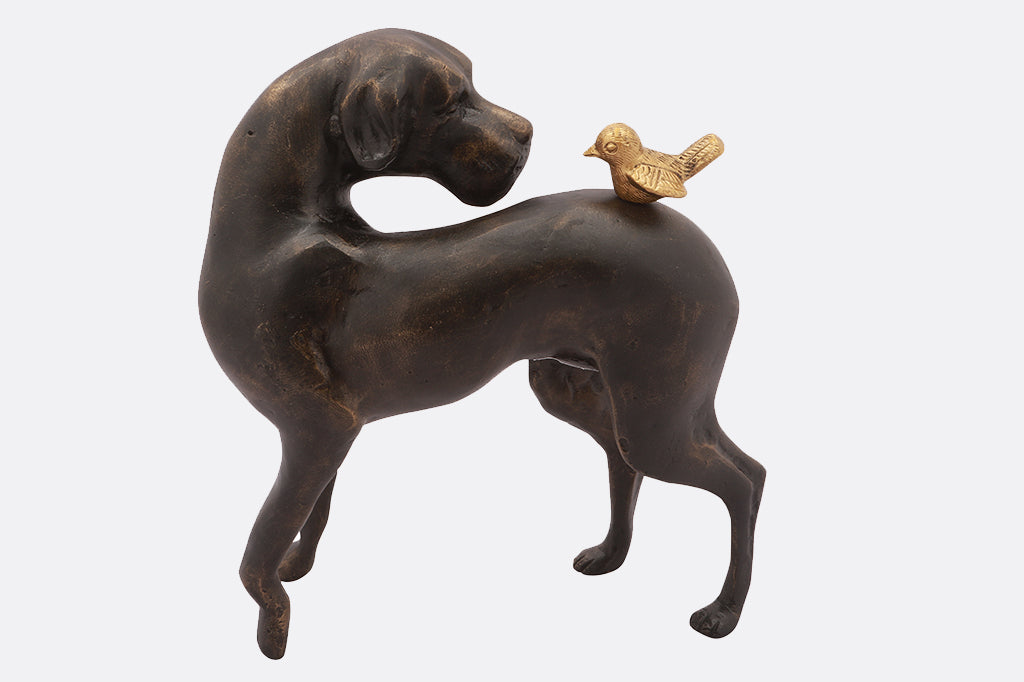 cast metal garden sculpture of dog looking at a bird on its back