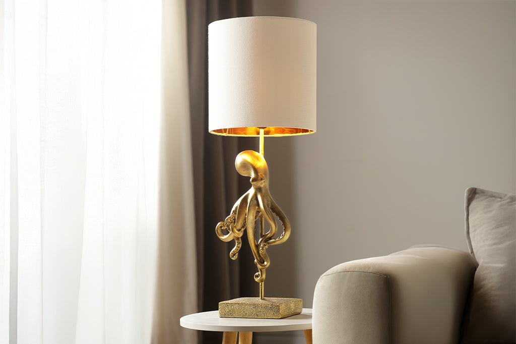 golden octopus lamp with white shade placed on side table next to neutral couch