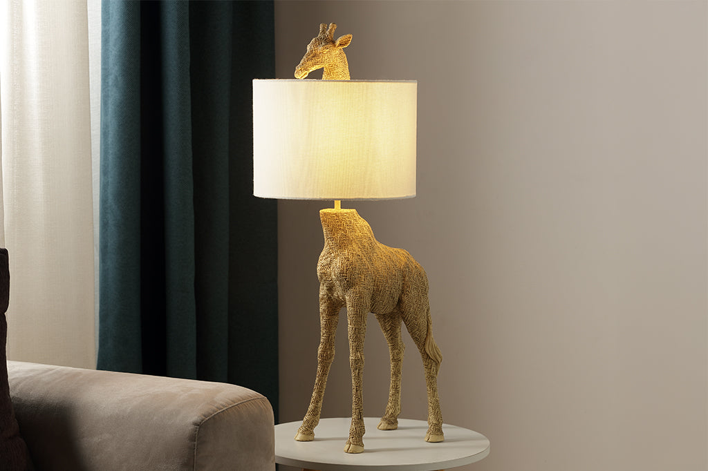 textured golden giraffe lamp with head poking out from top of white fabric shade set on small table lamp next to couch