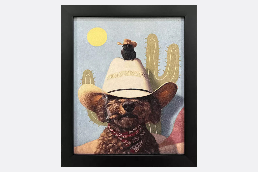 Framed artwork of a dog wearing a cowboy hat and a bird wearing a cowboy hat on top of him with a cactus and sun in the background.