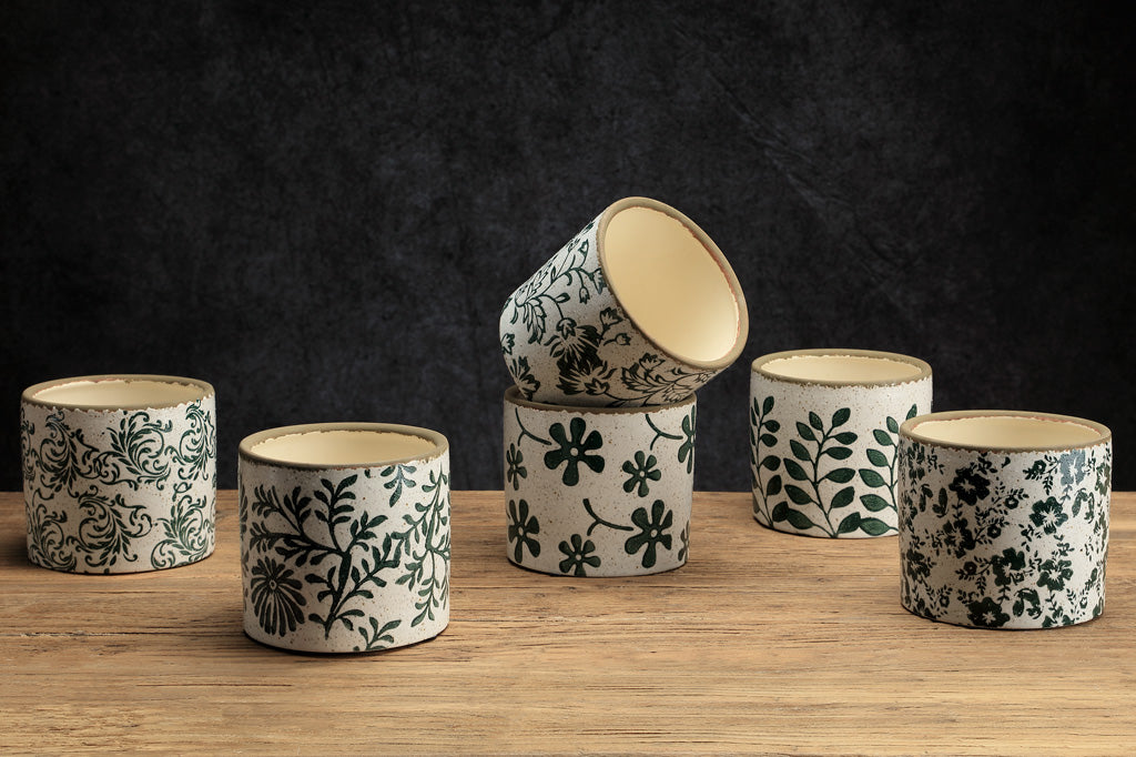 Set of ceramic pots with floral patterns on a wooden surface and dark background