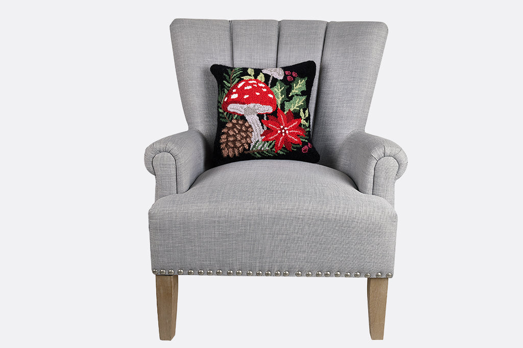 mushroom, pinecone, poinsettia, and holly leaves hooked pillow placed on gray armchair