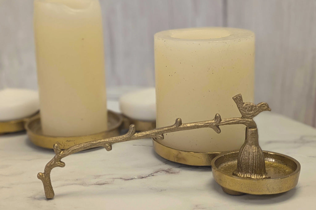 side view of antiqued bronze candle snuffer with bird and branch motif by pillar candles on table