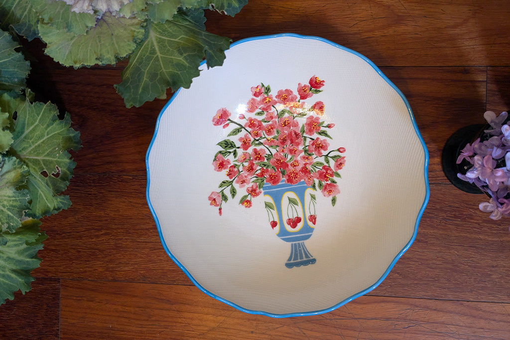 Stoneware bowl with scalloped edges painted in blue with floral arrangement in cheery vase - top view on a wood table with ornamental plants