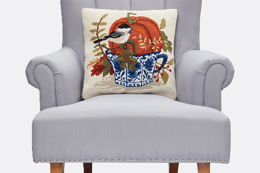 Decorative pillow with a bird and pumpkin design on a gray armchair