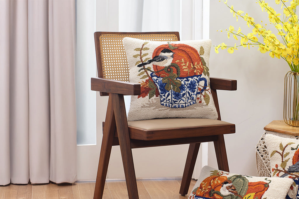 Wooden chair with decorative pillows featuring autumn-themed designs in a room with curtains and a vase of yellow flowers.