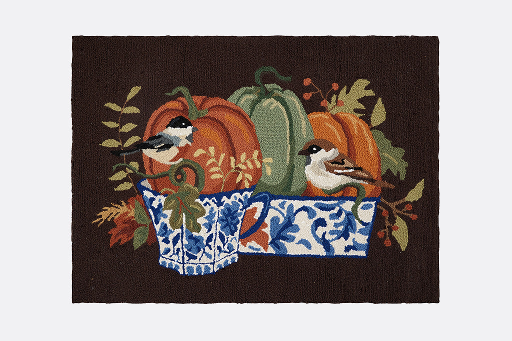 Decorative mat with pumpkins, birds, and a blue and white dish on a brown background