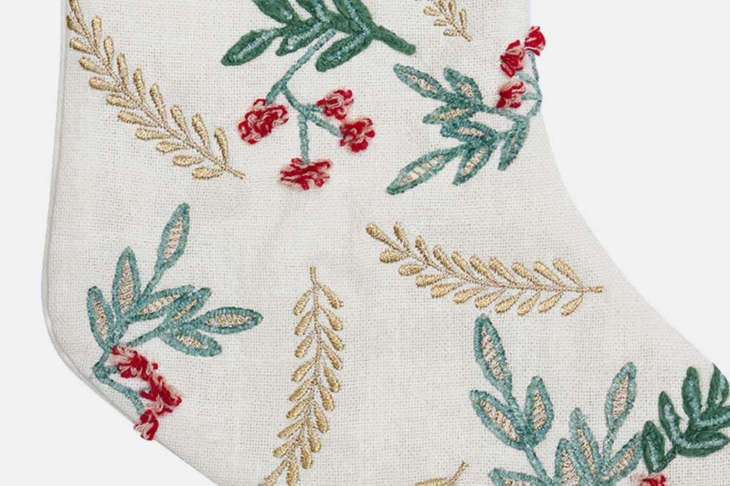 Close up detail of embroidered stocking with green leaves and red berries on a white background