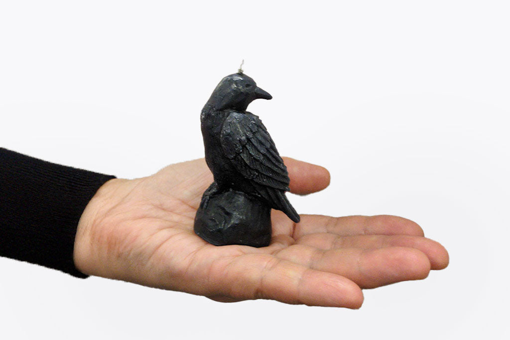 carved crow on rock figure in a candle, shown in palm of an outstretched hand