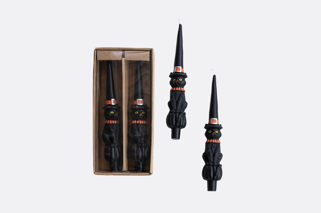 four taper candles, each featuring a black cat in a classic witch hat with bright orange details