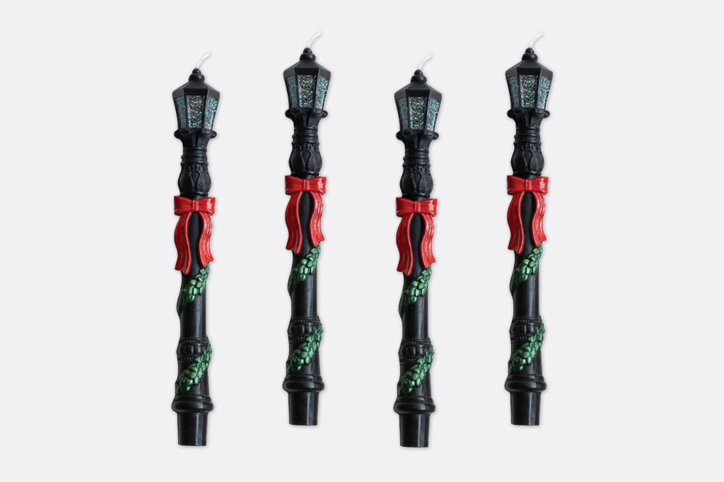 Four decorative candles of a lamp post with festive ribbons and greenery.
