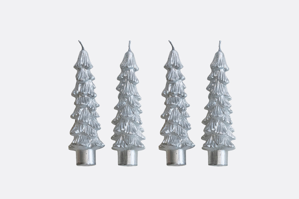 Four silver Christmas tree-shaped candles on a light gray background