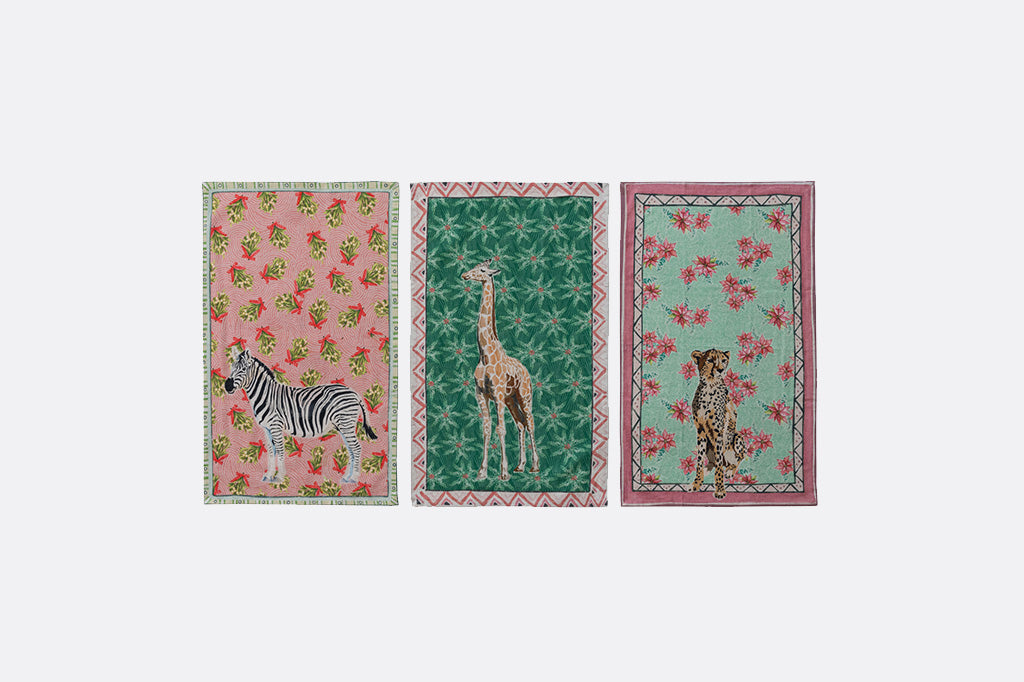 Three holiday tea towels with animal illustrations and festive prints. zebra, giraffe, cheetah