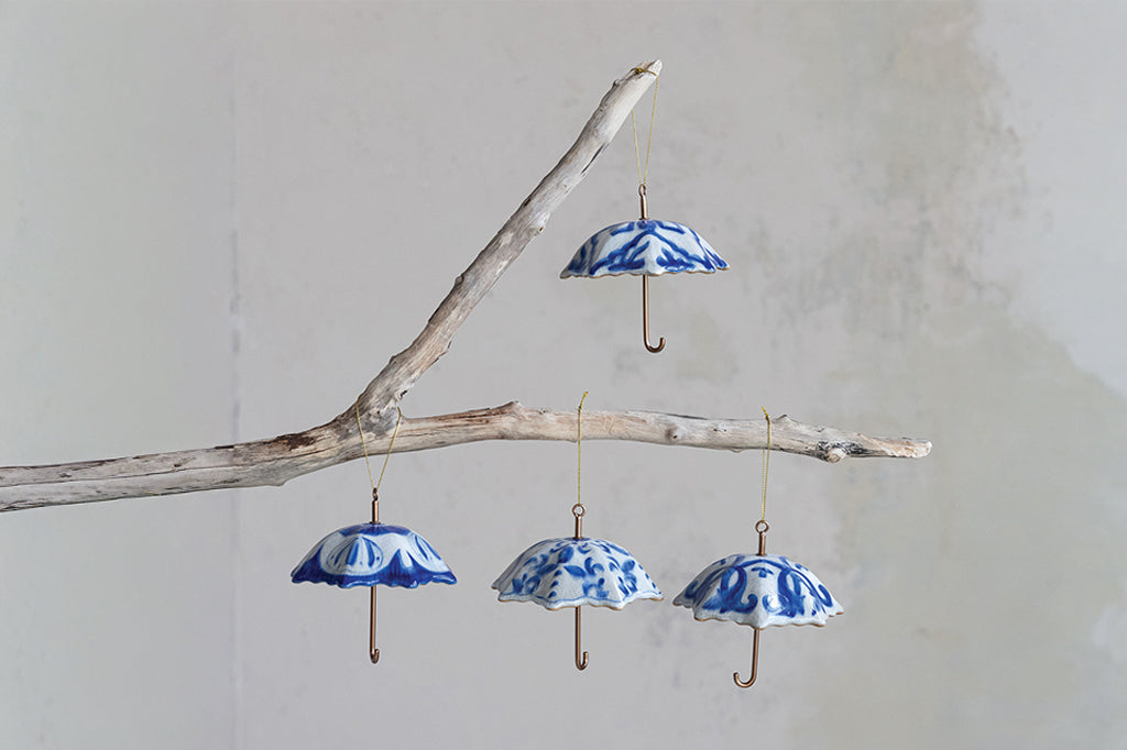 Blue and white ceramic umbrella decorations hanging from a branch against a light background