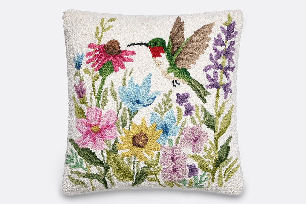 A hooked throw pillow featuring a green hummingbird and vibrant spring flowers.