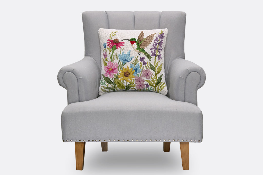 A hooked throw pillow featuring a green hummingbird and vibrant spring flowers.