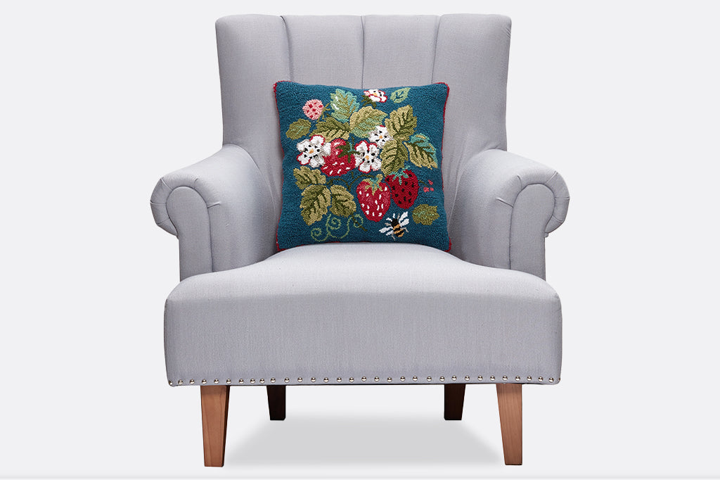A hooked pillow with illustrations of strawberries, flowers, leaves, and a bee.
