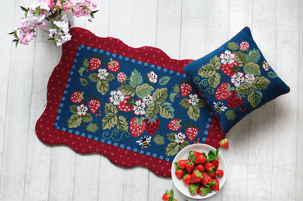Decorative floor mat and pillow with strawberry pattern on a white wooden surface.