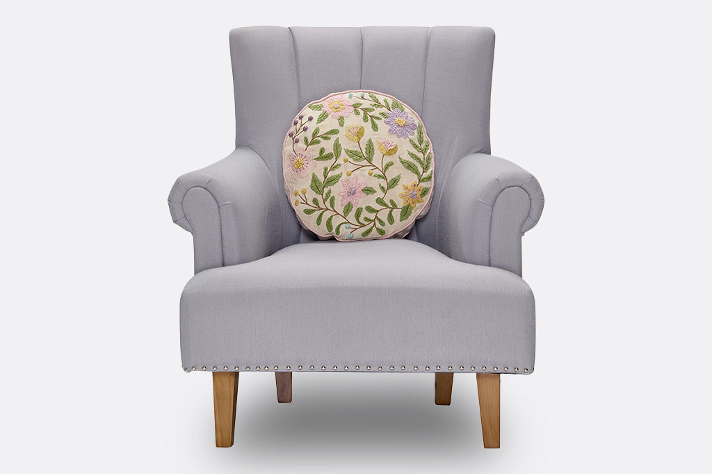 Round pillow with embroidered floral designs on a couch.