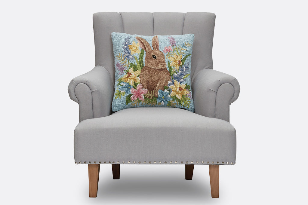Decorative pillow with a bunny and floral design on a light blue background on a chair