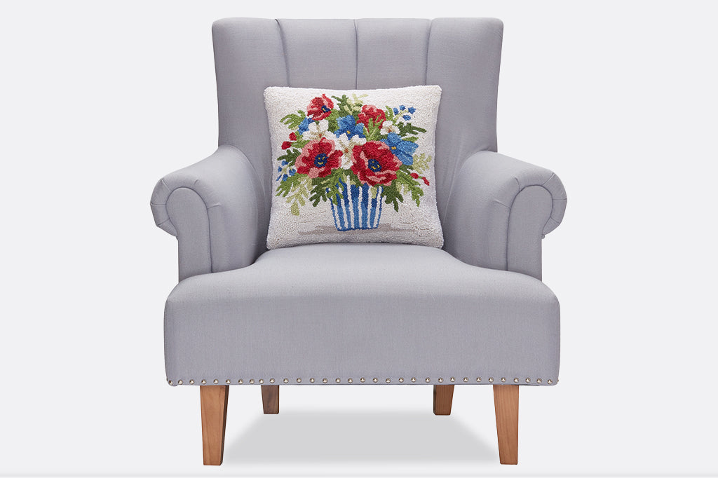 A hooked pillow of a bouquet of red, white, and blue flowers in a striped pot.
