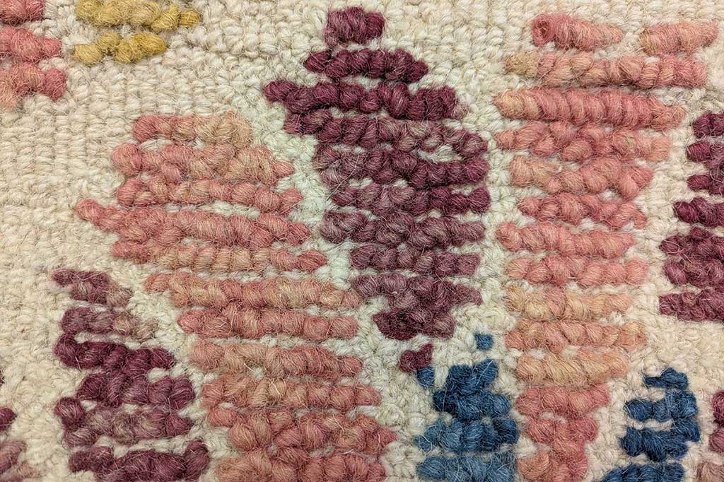 Close-up of a floral patterned wool rug with textural woven design on a stone color background