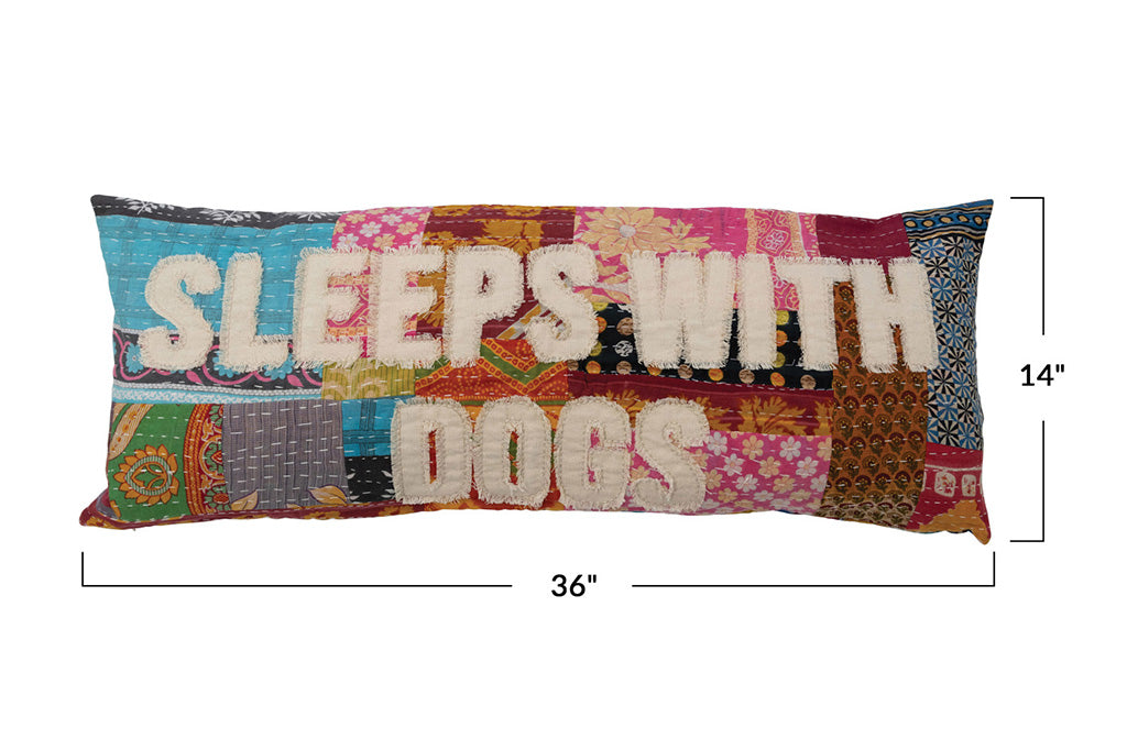 A patchwork pillow inscribed with the phrase "Sleeps with dogs."