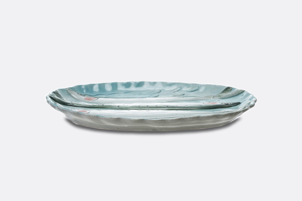 A light blue oval dish with three sardine fish illustrations.