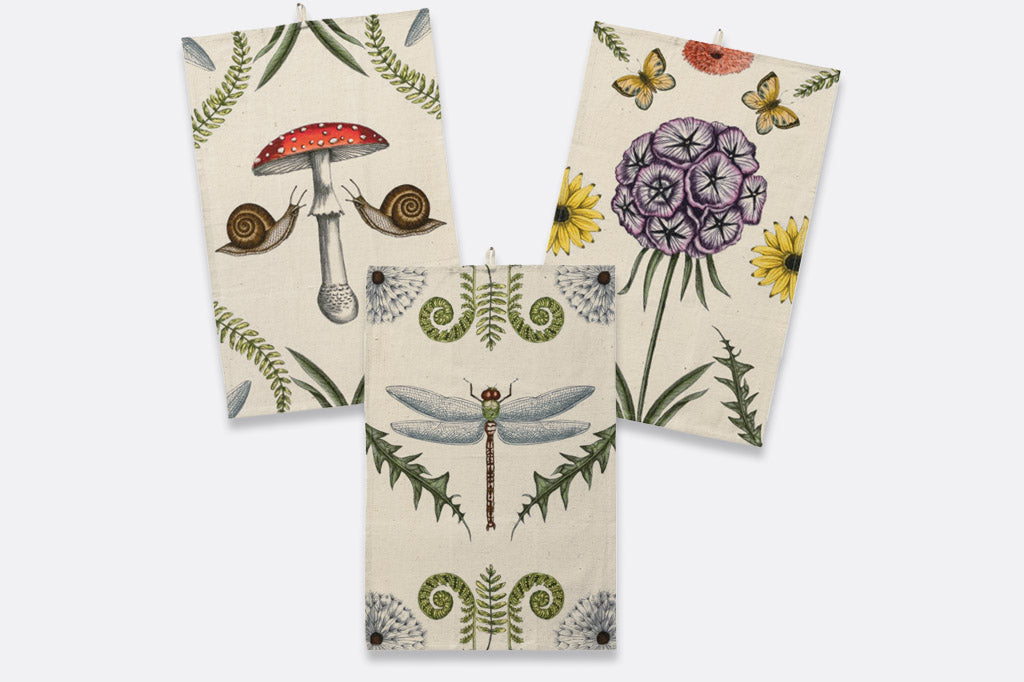 A set of 3 dish towels that have illustrations of mushrooms, butterflies, flowers, snails, and dragonflies.