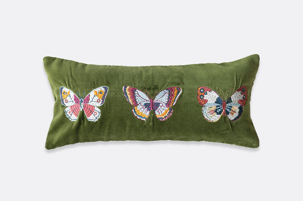 A green pillow with a beige back that has vibrantly colored butterflies embroidered onto it.