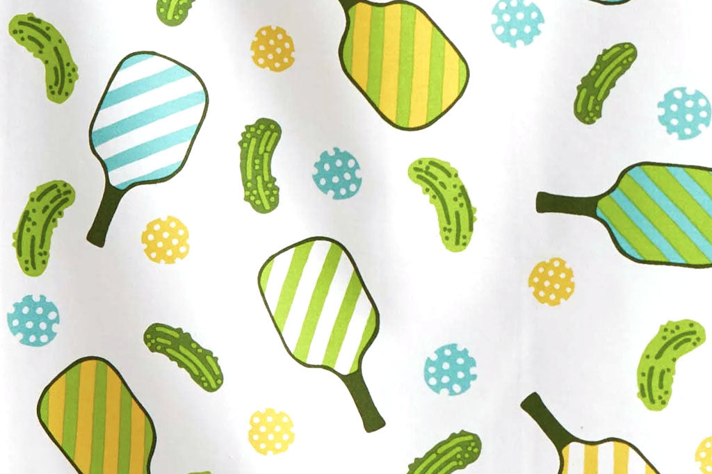 Pattern on tea towel of pickleball paddles and pickles on a white background