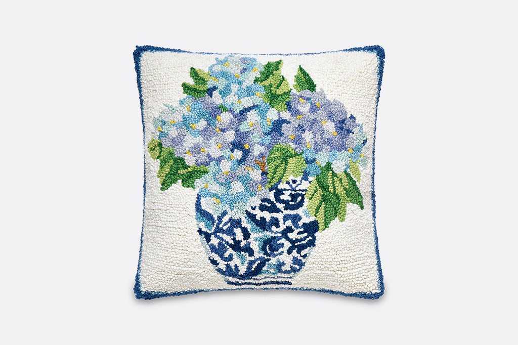 A hooked wool pillow with details of blue flowers in a vase.