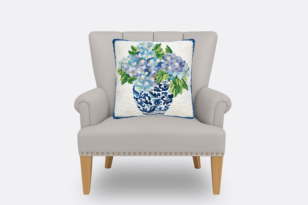 A hooked wool pillow with details of blue flowers in a vase.
