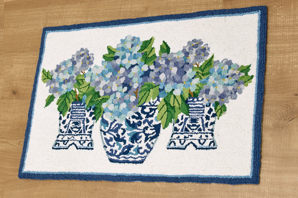 A blue and white hooked rug with illustrations of 3 vases with blue flowers with green leaves.