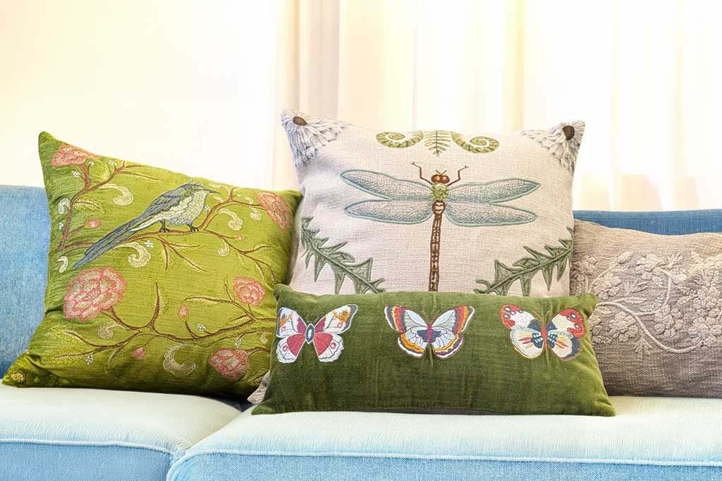 Decorative pillows with floral, butterfly, and dragonfly patterns on a couch.