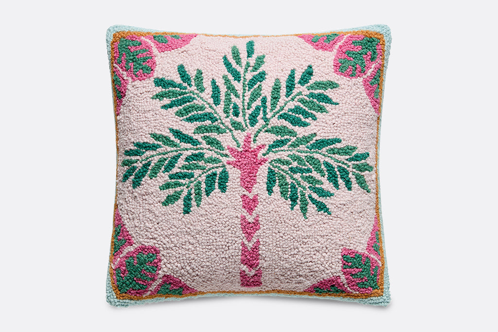A hooked pillow with vibrant pink, orange, green, blue illustrations of palm trees and leaves.