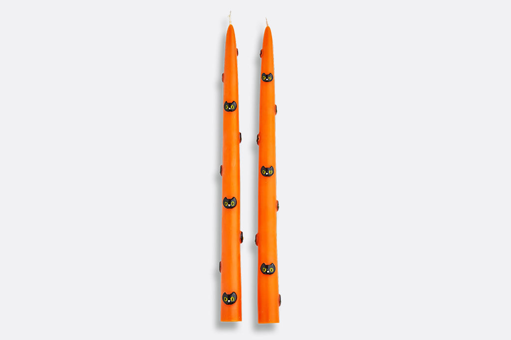 Two orange candles with black cat designs on a white background
