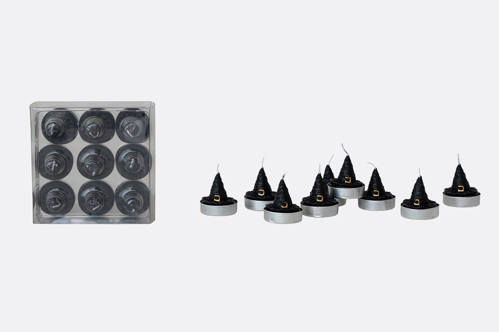 Set of black candles with pointed tops and a clear container of unlit candles on a white background