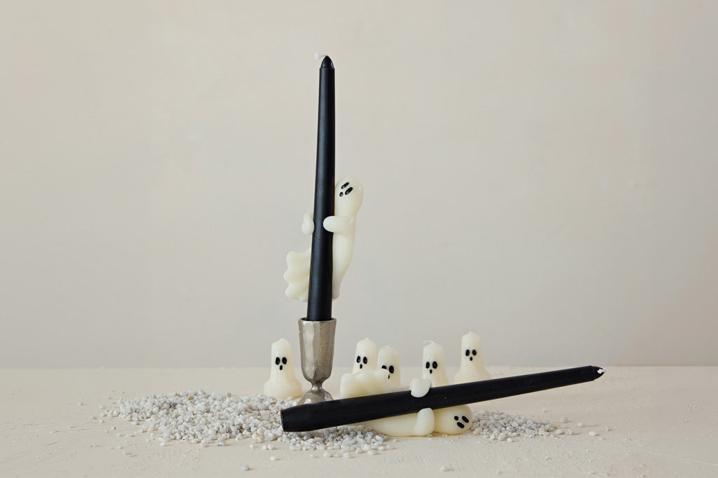 Two black candles with ghost-shapes on a light gray surface.