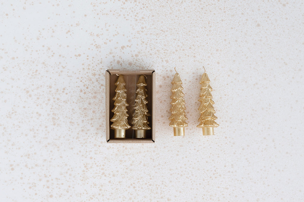 Four gold Christmas tree-shaped candles, with two inside a small brown box and two standing beside it, on a light speckled background.