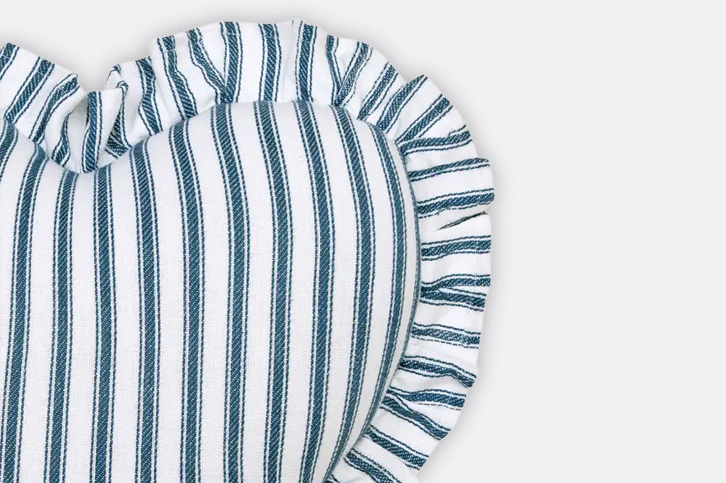 A white ruffle heart shaped pillow with blue stripes.