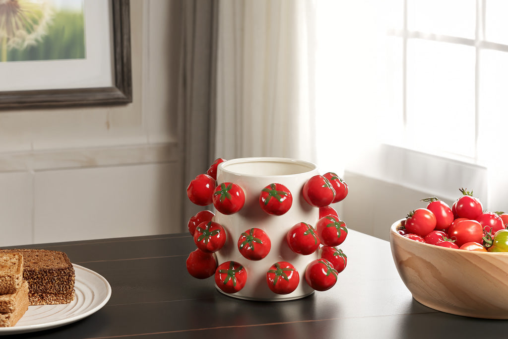 Decorative vase with tomato design on a table with a sliced bread and bowl of tomatoes