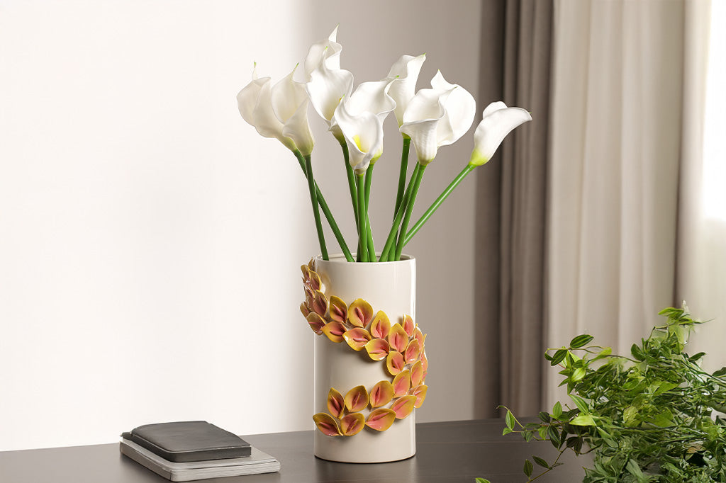 White vase with floral design on a table with white flowers.