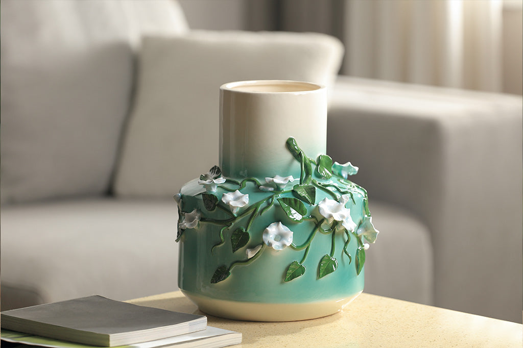 A vase with a green colorway and a design of vines and blossoming flowers.