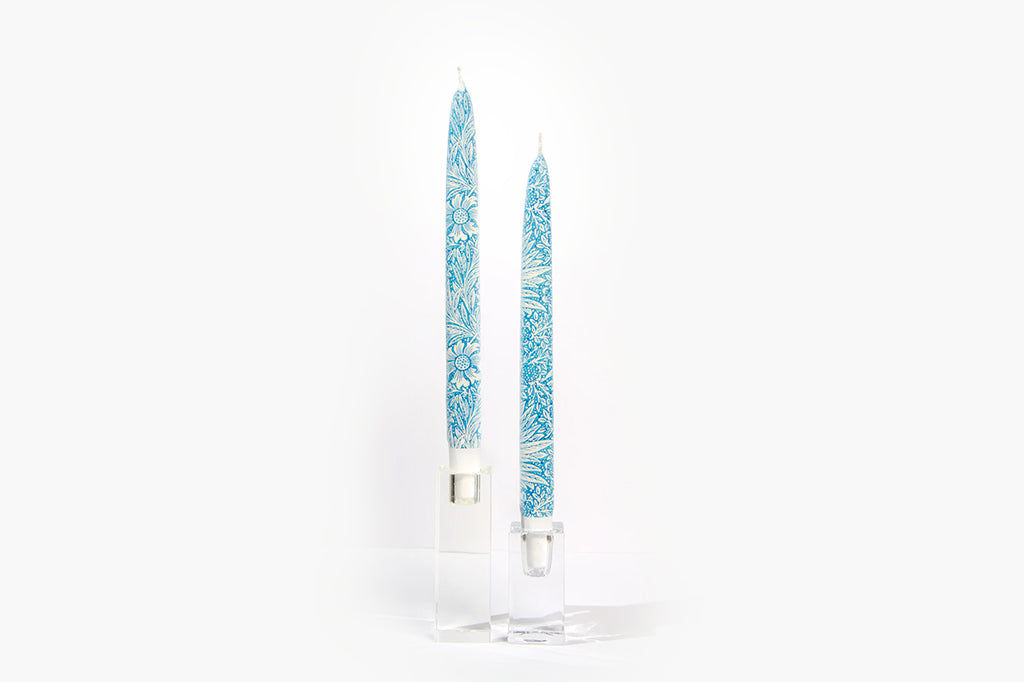 Two blue patterned taper candles in glass candle holders on a white background