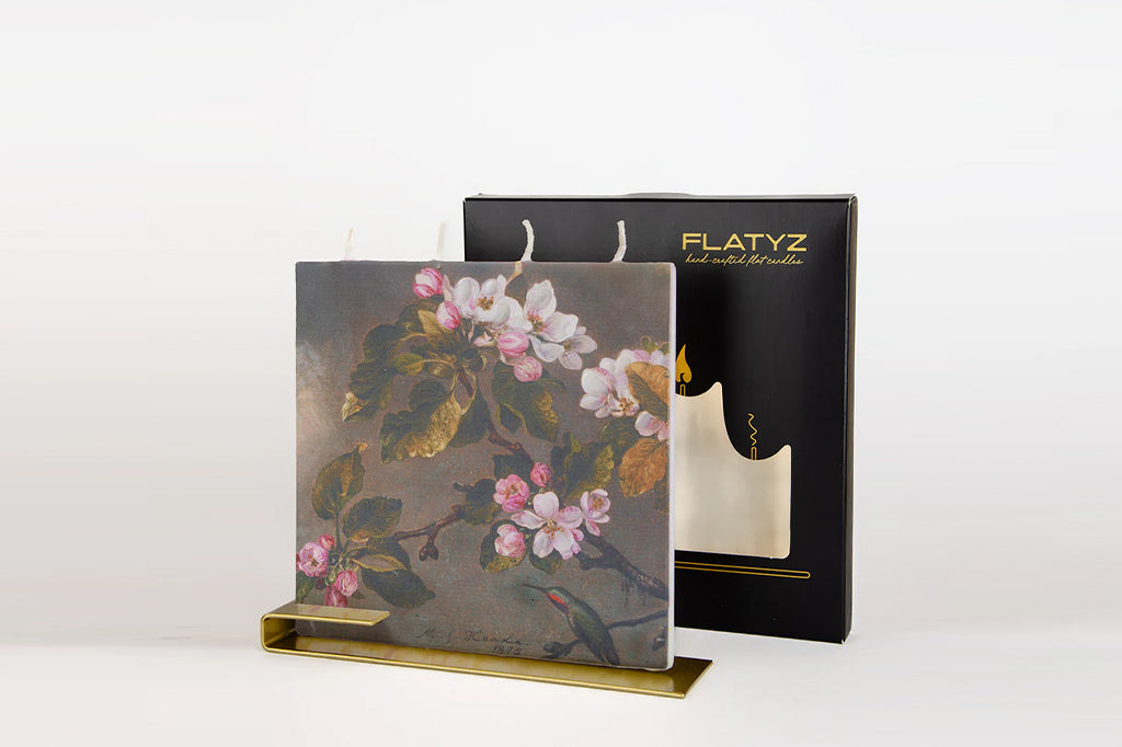 Decorative square flat candle with four wicks and floral design, shown on a steel stand, next to a FLATYZ branded box.